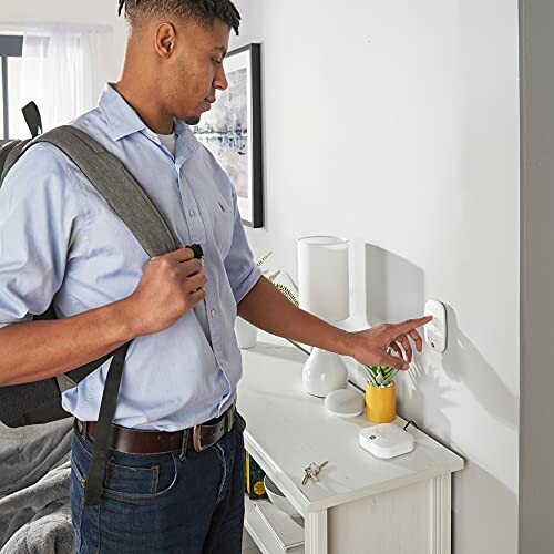 Man adjusting smart thermostat on wall near a table with a plant.