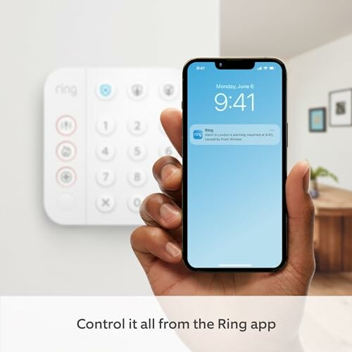 Hand holding smartphone with Ring app notification, keypad in background.